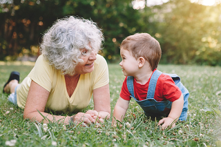 An older woman on the grass with a small child, facing each other and talking.